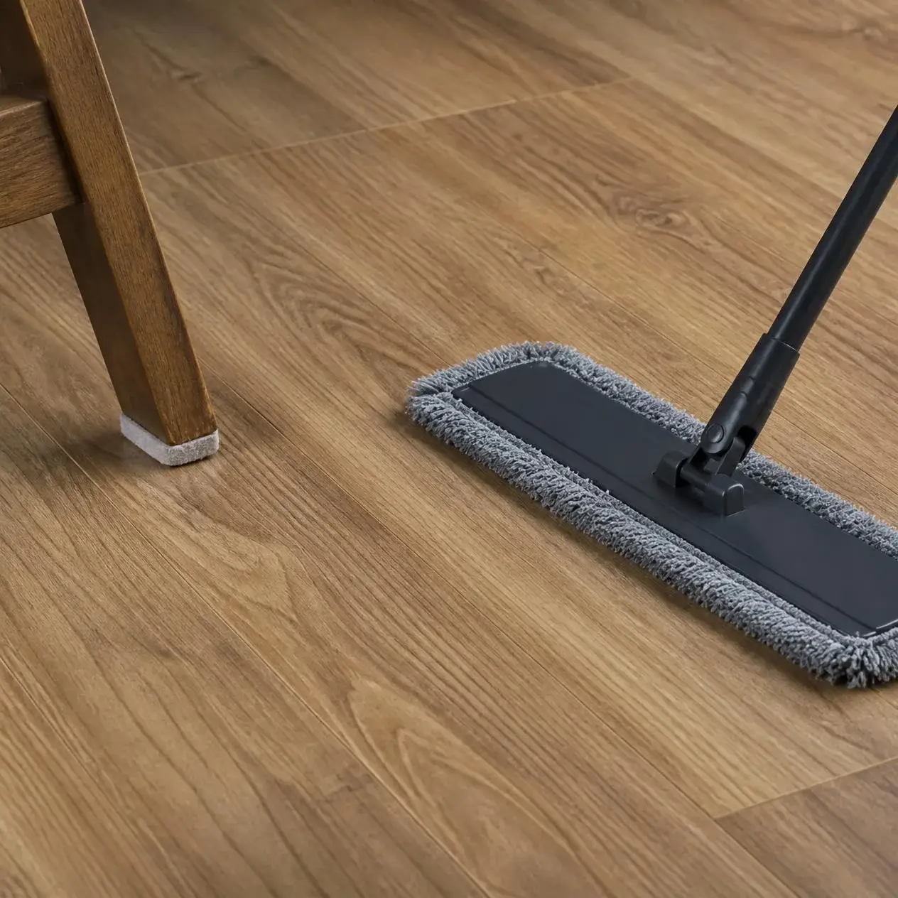 Microfiber dust mop on a matte oak-look laminate floor next to a chair leg with a felt pad