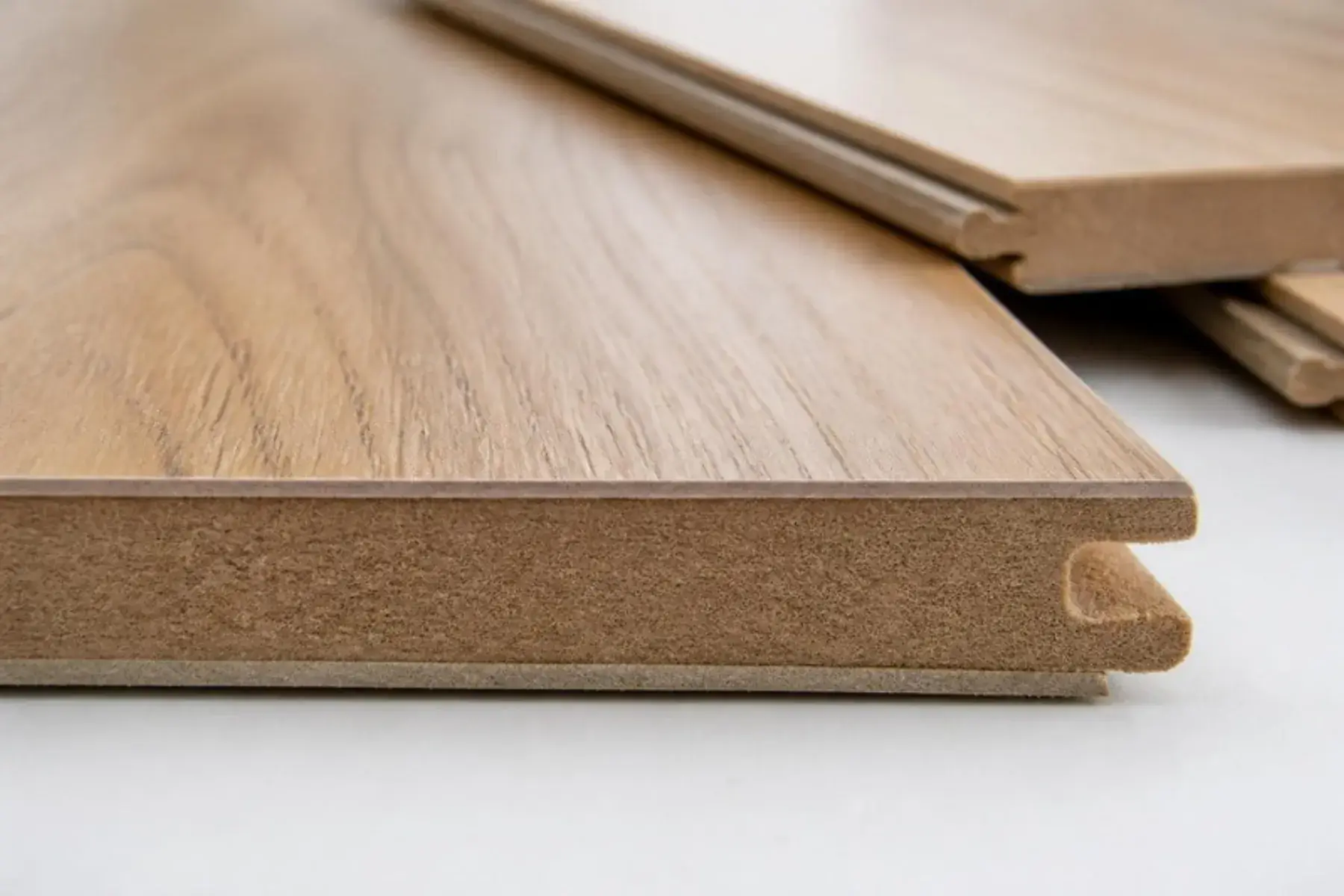 Close-up of a laminate plank edge showing the wear layer, printed oak decor layer, HDF core and click-lock profile