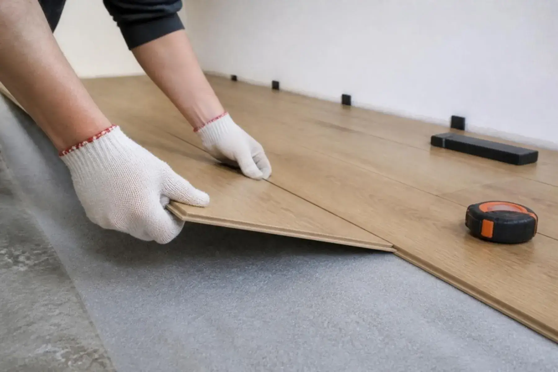 Installer clicking an oak-look laminate plank into place over foam underlayment on a concrete slab