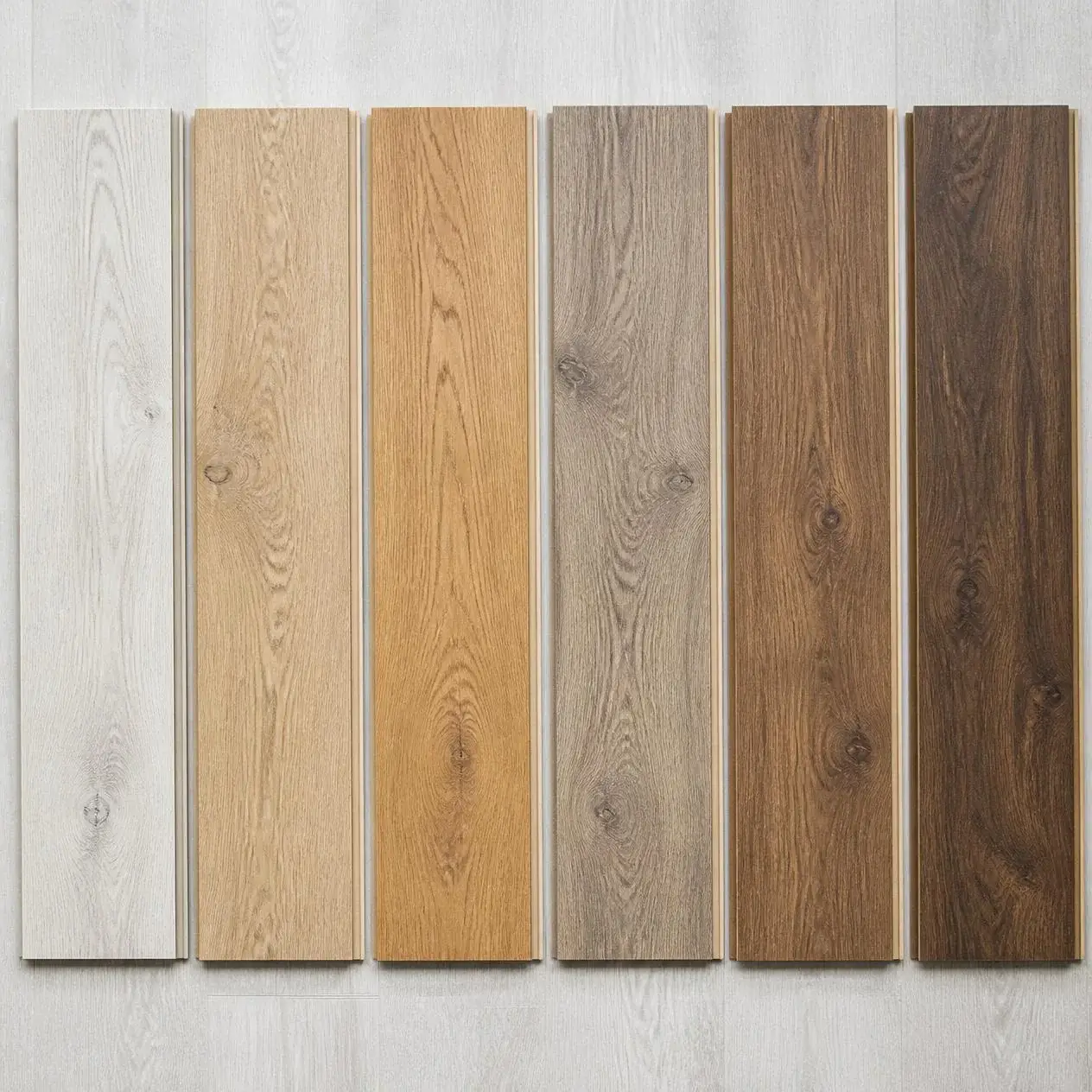 Six laminate flooring samples from whitewashed oak to dark walnut laid side by side for comparison