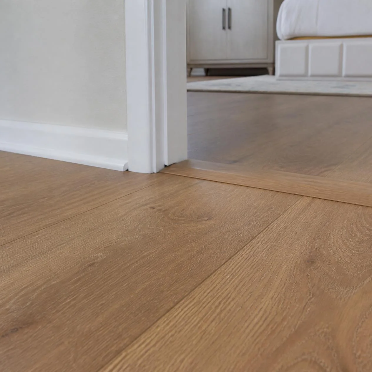 Finished laminate flooring with white baseboard, quarter-round trim and a color-matched doorway transition