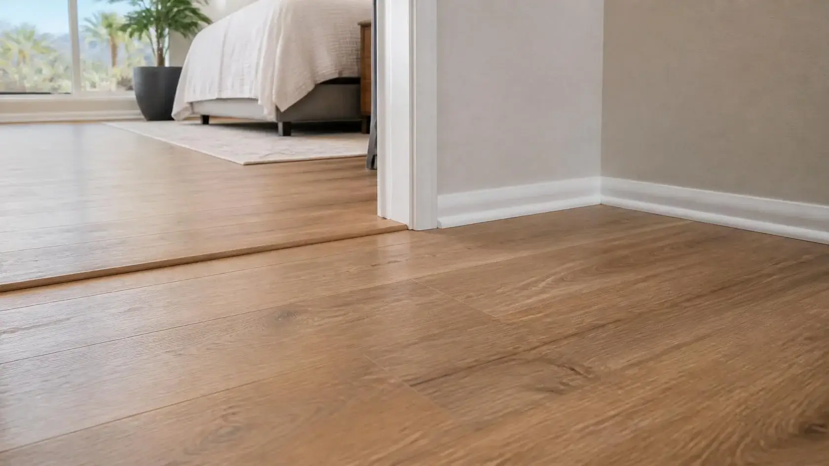 Finished laminate flooring with white baseboard, quarter-round trim and a color-matched doorway transition