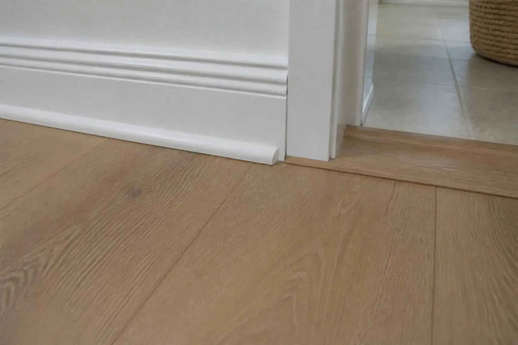 Finished laminate flooring with white baseboard, quarter-round trim and a color-matched doorway transition